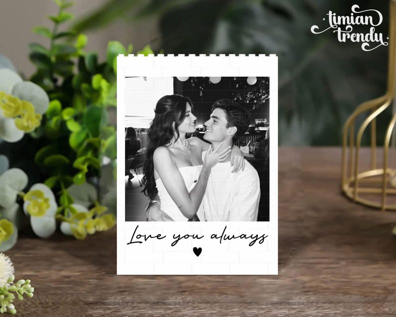 Puede incluir: Un bloque rectangular blanco con un borde de patr&oacute;n de ladrillo que presenta una fotograf&iacute;a en blanco y negro de una pareja abraz&aacute;ndose. Debajo de la foto, el texto Love you always aparece en una fuente cursiva negra, seguido de un coraz&oacute;n.