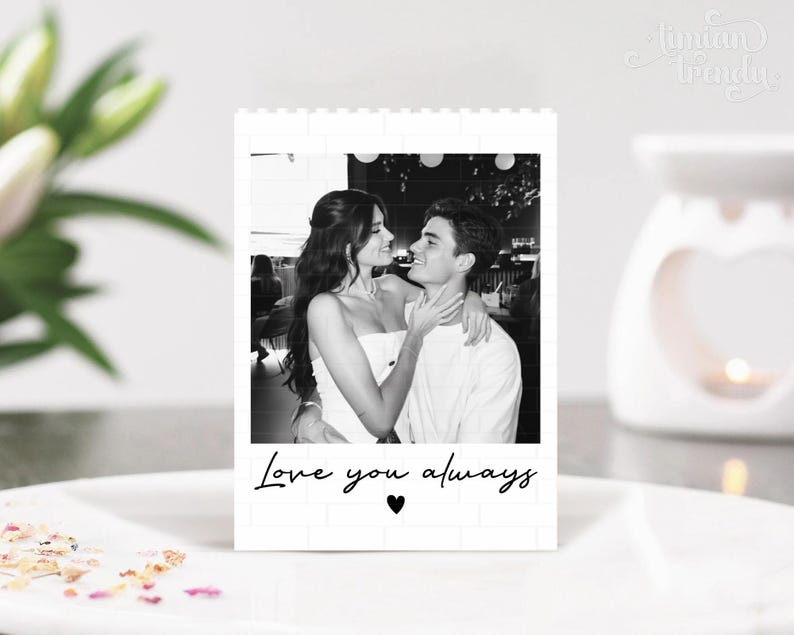 Puede incluir: Un bloque rectangular blanco con un borde de patr&oacute;n de ladrillo que presenta una fotograf&iacute;a en blanco y negro de una pareja abraz&aacute;ndose. El texto Love you always est&aacute; impreso en cursiva negra debajo de la foto, seguido de un peque&ntilde;o coraz&oacute;n.