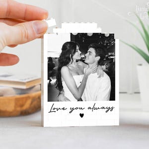 Puede incluir: Un marco rectangular de bloques de construcci&oacute;n blancos con una fotograf&iacute;a en blanco y negro de una pareja abraz&aacute;ndose. El texto Love you always est&aacute; impreso en letra cursiva negra debajo de la foto, seguido de un peque&ntilde;o coraz&oacute;n negro en el centro.