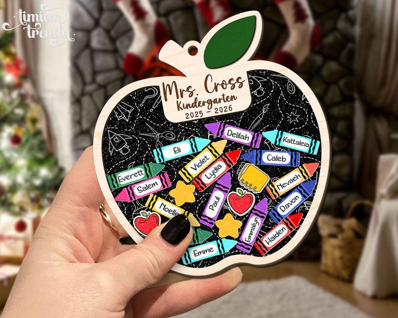 May include: Wooden apple-shaped ornament with a chalkboard design. It features the text "Mrs. Cross Kindergarten 2025-2026" and crayon illustrations with student names. A green leaf tops the apple.
