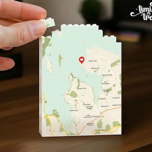 May include: A rectangular building block structure featuring a printed map of the Great Neck and Port Washington area. The map displays light green water, tan land, yellow roads, and a red heart-shaped location pin over Sands Point.