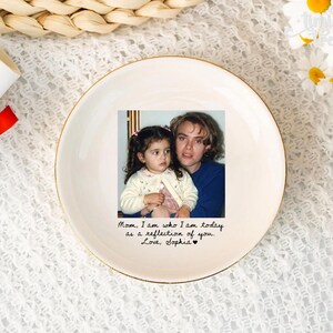 May include: A round white ceramic trinket dish with a gold-colored rim. The center features a color photograph of a child and an adult, with the printed text: Mom, I am who I am today as a reflection of you. Love, Sophia, followed by a small heart.