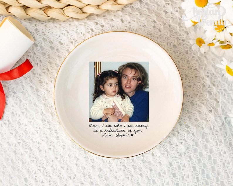 May include: A round white ceramic trinket dish with a gold-colored rim. The center features a color photograph of a child and an adult, with the printed text: Mom, I am who I am today as a reflection of you. Love, Sophia, followed by a small heart.