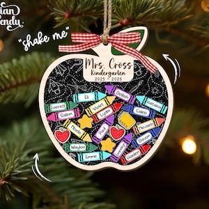 May include: Wooden apple-shaped ornament with a chalkboard design. The ornament features the text "Mrs. Cross Kindergarten 2025-2026" and includes colorful crayon and apple illustrations. It is decorated with a red and white ribbon and a jute string for hanging.