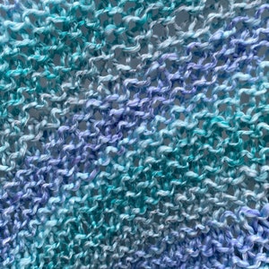Op de afbeelding: Close-up van een gebreide stof met een gradi&euml;nt van blauwe en paarse kleuren. De stof is gemaakt van een zacht, getextureerd garen en heeft een losse, open weving.