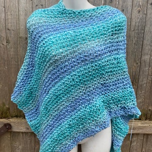 Op de afbeelding: Een blauwe en groene gebreide poncho met een losse, open structuur. De poncho is over een wit mannequin gehangen.