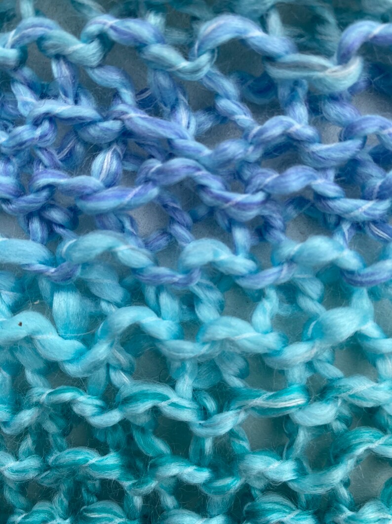 Op de afbeelding: Close-up van een gebreide stof met een gradi&euml;nt van blauwe en turquoise garen. De stof is gemaakt met een eenvoudig steekpatroon, waardoor een textuur ontstaat.