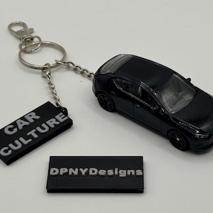 May include: Black diecast car keyring with a silver ring and chain. Includes a black rectangular tag with "CAR CULTURE" in white lettering. A second black tag with "DPNYDesigns" is also present.
