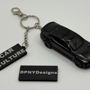 Può includere: Portachiavi per auto modello pressofuso nero con catena argentata ed etichetta rettangolare con la scritta "CAR CULTURE". Una seconda etichetta recita "DPNYDesigns".