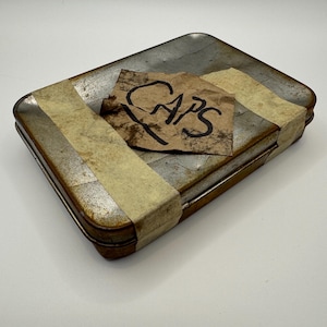 May include: A rusty metal box with a brown paper label that says "CAPS" taped to the top. The box is wrapped with tan tape.