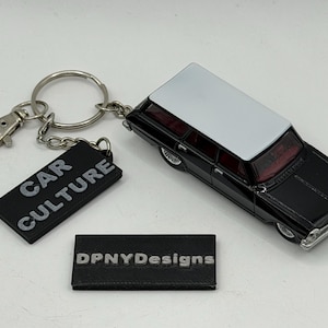 May include: A keychain featuring a miniature black and white station wagon car model with a silver metal ring and lobster clasp. Attached is a black rectangular tag with the embossed grey text CAR CULTURE. A separate black tag displays DPNYDesigns.