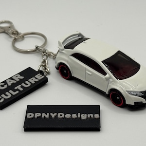 May include: White car keychain with black and red accents. The keychain includes a black rectangular tag with the words "CAR CULTURE" and another tag with "DPNYDesigns".