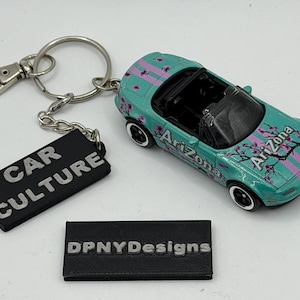 May include: A teal toy car with Arizona graphics and a keychain with a black tag that reads "CAR CULTURE". The car has black wheels and a black interior. A second black tag reads "DPNYDesigns".