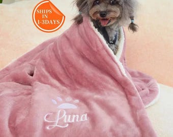 Puede incluir: Una manta rosa para perro con una huella de pata blanca y el nombre "Luna" bordado. Un perro pequeño está acurrucado dentro de la manta.