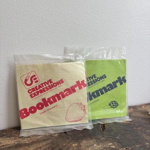 May include: Two Creative Expressions bookmark craft kits in clear plastic packaging. The left kit has a cream background with red text and a strawberry illustration. The right kit has a light green background with black text and a ladybug illustration.