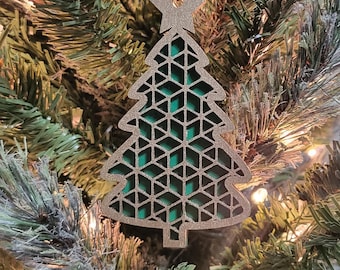 May include: A gold and green Christmas tree ornament with a geometric design. The ornament is hanging on a green artificial Christmas tree.