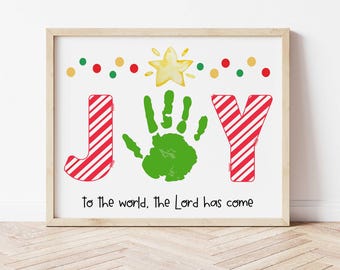 May include: A framed print with a red and white striped "JOY" design. The "O" is a green handprint. The print has a yellow star and red and green polka dots at the top. The text "To the world, the Lord has come" is at the bottom.