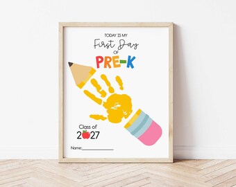 May include: A framed print with the text "TODAY IS MY First Day of PRE-K" in colorful letters. A yellow handprint is incorporated into a pencil design. The print also includes "Class of 2027" and a space for a name.
