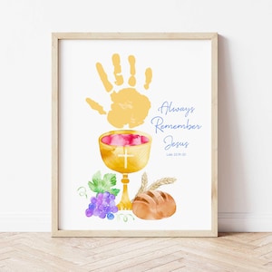 May include: Framed watercolour print with a handprint, chalice, grapes, and bread. The text reads "Always Remember Jesus" with the reference Luke 22:19-20. The artwork is in a wooden frame, suitable for home decor.