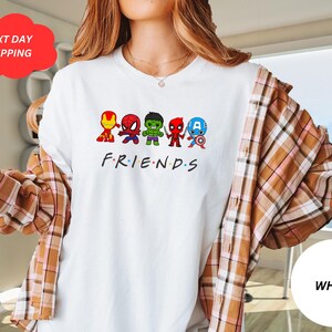 Puede incluir: Camiseta blanca con un gr&aacute;fico de superh&eacute;roes de dibujos animados, incluyendo Spider-Man, Hulk, Iron Man, Capit&aacute;n Am&eacute;rica y Thor. El texto "FRIENDS" est&aacute; debajo del gr&aacute;fico.