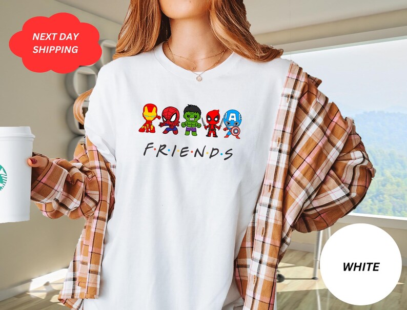 Puede incluir: Camiseta blanca con un gr&aacute;fico de superh&eacute;roes de dibujos animados, incluyendo Spider-Man, Hulk, Iron Man, Capit&aacute;n Am&eacute;rica y Thor. El texto "FRIENDS" est&aacute; debajo del gr&aacute;fico.