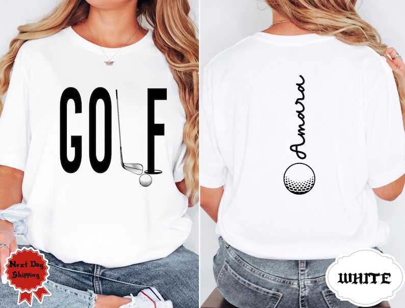 May include: White t-shirt with the word "GOLF" in large black letters on the front, along with a golf club, ball, and hole graphic. The back of the shirt features the name "Amara" in a vertical script above a golf ball graphic.