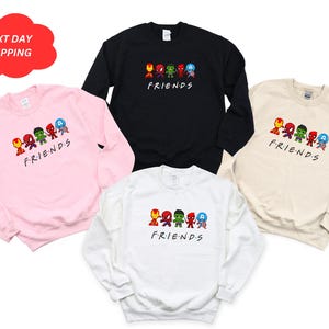 Pu&ograve; includere: Quattro felpe con collo rotondo in rosa, nero, beige e bianco con una grafica di supereroi dei cartoni animati in fila con la parola "FRIENDS" sotto.