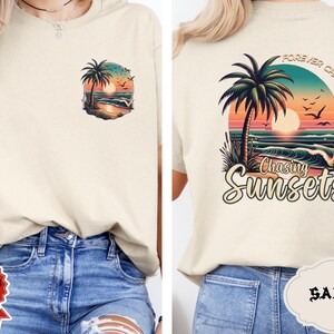 May include: Sand-colored t-shirt with a tropical sunset design. The front features a small graphic of a palm tree, sunset, and ocean. The back displays a larger design with the text "Forever Chasing Sunsets" and "Chasing Sunsets".