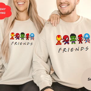Pu&ograve; includere: Due felpe color crema con un'immagine di supereroi dei cartoni animati e il testo "FRIENDS".