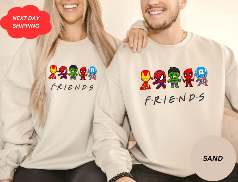 Pu&ograve; includere: Due felpe color crema con un'immagine di supereroi dei cartoni animati e il testo "FRIENDS".