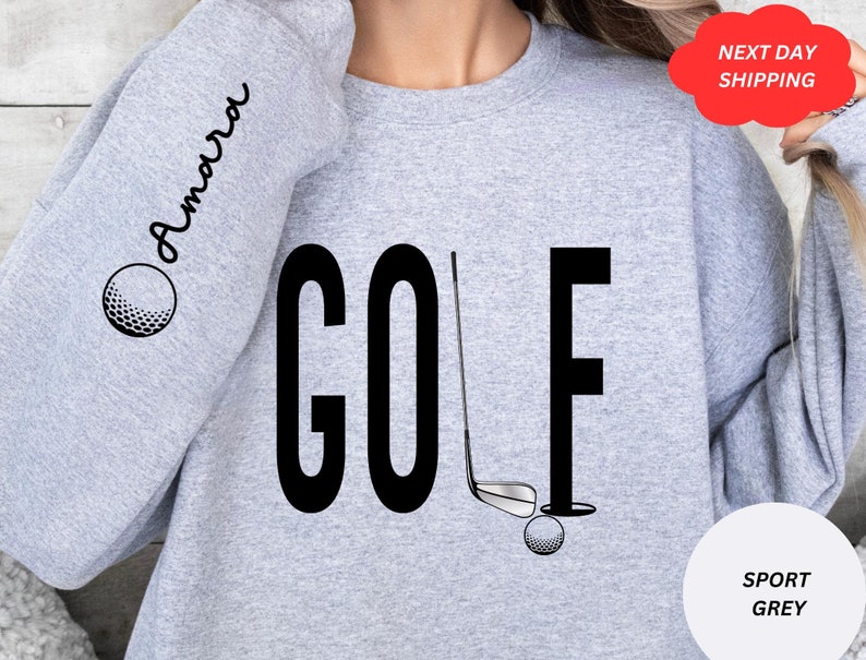 Pu&ograve; includere: Felpa grigia con la parola "GOLF" stampata in nero. La parola &egrave; stilizzata con una mazza da golf e una palla. La manica ha la parola "Amarra" stampata in corsivo.