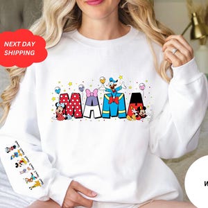 Puede incluir: Sudadera blanca con un gr&aacute;fico de Mickey Mouse, Minnie Mouse, Donald Duck y Goofy deletreando "MAMA" con globos y estrellas de colores.