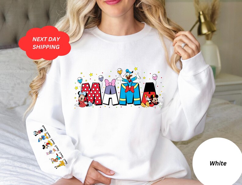 Puede incluir: Sudadera blanca con un gr&aacute;fico de Mickey Mouse, Minnie Mouse, Donald Duck y Goofy deletreando "MAMA" con globos y estrellas de colores.