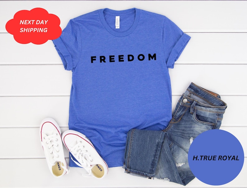 May include: A blue t-shirt with the word "FREEDOM" in black block letters. The shirt is paired with blue jeans and white sneakers with red accents. A red cloud-shaped graphic reads "NEXT DAY SHIPPING".