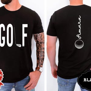 May include: Black t-shirt with the word "GOLF" in large white letters and a golf club graphic. The back of the shirt features the name "Amara" in white script above a golf ball graphic. The shirt is black.