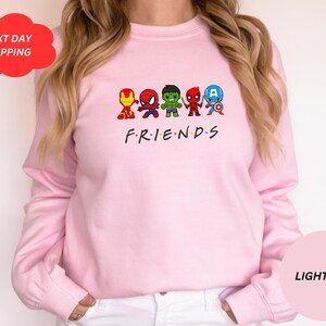 Pu&ograve; includere: Felpa rosa chiaro con una grafica di cinque supereroi dei cartoni animati, tra cui Iron Man, Spiderman, Hulk, Thor e Captain America. Il testo "FRIENDS" &egrave; stampato sotto i supereroi.