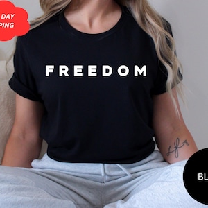 May include: Black t-shirt with the word "FREEDOM" printed in white. The shirt has short sleeves and a round neckline. A black circle with the word "BLACK" is in the lower right corner.