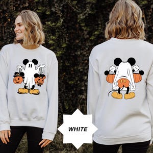 May include: White sweatshirt featuring a Halloween-themed Mickey Mouse design. The front graphic shows Mickey as a ghost holding jack-o'-lanterns. The back graphic shows Mickey Mouse with a ghost sheet and pumpkins. The word "WHITE" is in a white starburst.