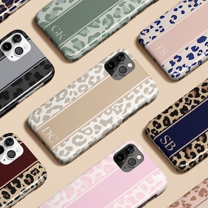 以下が含まれることがあります： さまざまなヒョウ柄デザインのスマートフォンケースのコレクション。ケースは、イニシャル入りの中央ストライプが特徴で、グレー、タン、ピンク、ネイビーなどの色があります。モダンな美学のために設計されています。