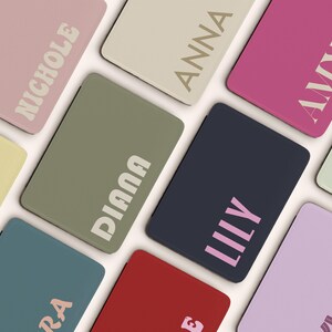 May include: A collection of colorful rectangular cases, each with a different name printed on it. The cases are in various colors, including pink, green, blue, and red. The names are in a contrasting font.