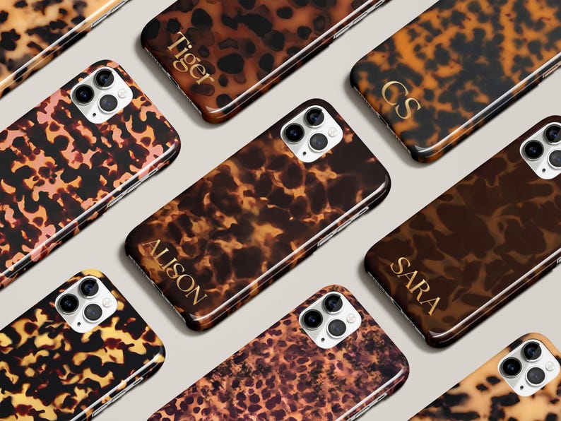 May include: A collection of tortoiseshell-patterned phone cases. The cases feature a variety of brown and tan hues, with some displaying personalized gold lettering. The cases are designed to fit a smartphone with a multi-lens camera.