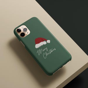 May include: A green phone case featuring a red and white Santa hat illustration and the words "Merry Christmas" in a handwritten style. The case is designed for a smartphone.