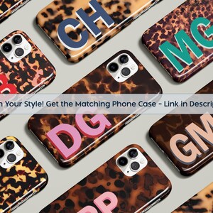 Op de afbeelding: Een verzameling telefoonhoesjes met een schildpadpatroon. Elke hoes heeft initialen in verschillende kleuren. De tekst "Match Your Style! Get the Matching Phone Case - Link in description" is zichtbaar.
