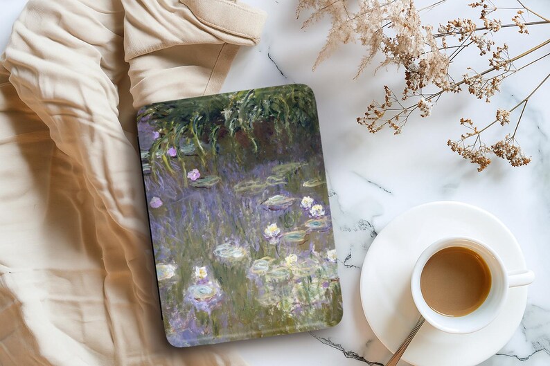 Może przedstawiać: Etui na tablet z obrazem w stylu Moneta przedstawiającym lilie wodne w stawie, w odcieniach zieleni, fioletu i bieli. Na marmurowej powierzchni, obok filiżanki kawy i suszonych kwiat&oacute;w.