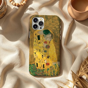 May include: A phone case featuring Gustav Klimt's "The Kiss" artwork. The case displays the iconic painting with its gold, yellow, and green hues. The design is set against a textured background, showcasing the artwork's details.