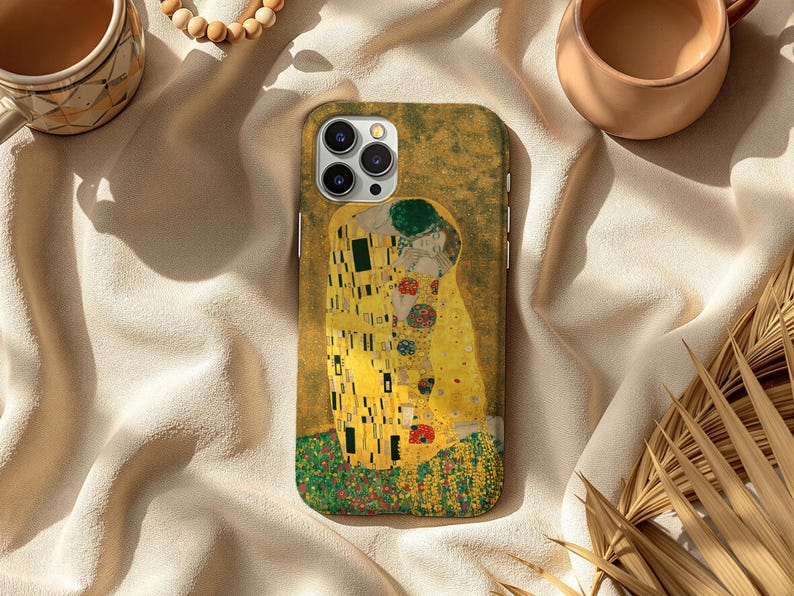 May include: A phone case featuring Gustav Klimt's "The Kiss" artwork. The case displays the iconic painting with its gold, yellow, and green hues. The design is set against a textured background, showcasing the artwork's details.