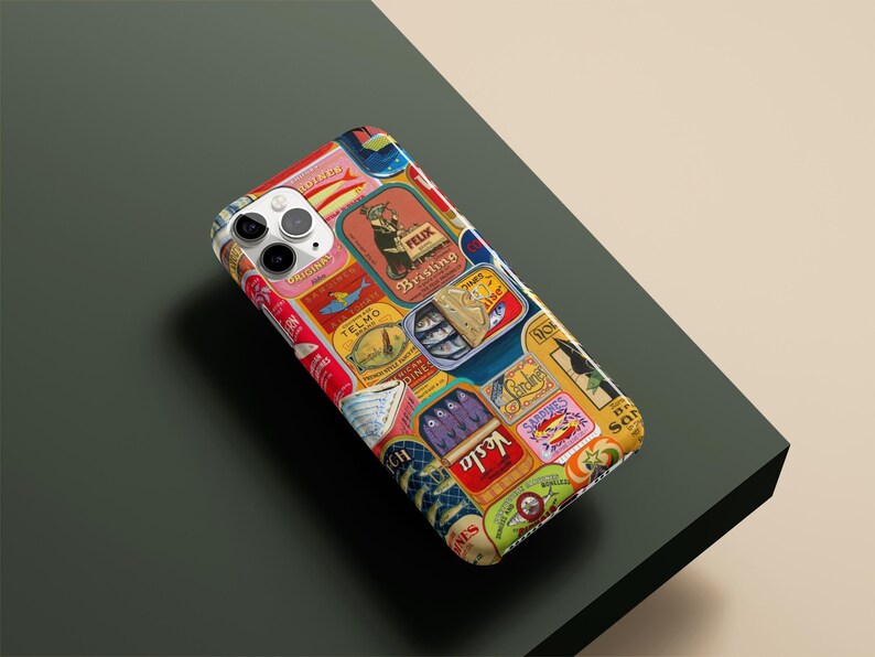 Może przedstawiać: Etui na smartfon z kolażem etykiet z puszek po sardynkach w stylu vintage. Etykiety są w r&oacute;żnych kolorach, w tym czerwonym, ż&oacute;łtym, niebieskim i zielonym, z tekstem i ilustracjami. Etui leży na ciemnozielonej powierzchni.