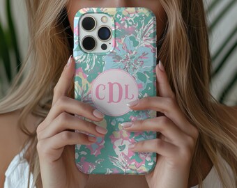 May include: A smartphone case featuring a vibrant floral pattern in shades of teal, light blue, pink, and yellow. The center of the case displays a circular white emblem containing the pink monogram letters CDL in a decorative script font.