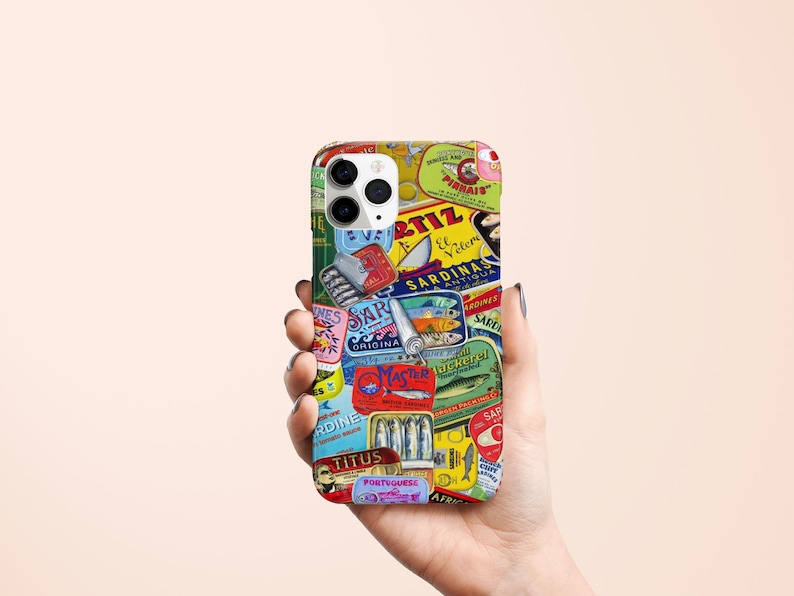 Może przedstawiać: Etui na telefon z kolażem etykiet po puszkach sardynek w stylu vintage w r&oacute;żnych kolorach. Etykiety zawierają tekst i ilustracje, tworząc estetykę retro. Etui jest trzymane w dłoni.