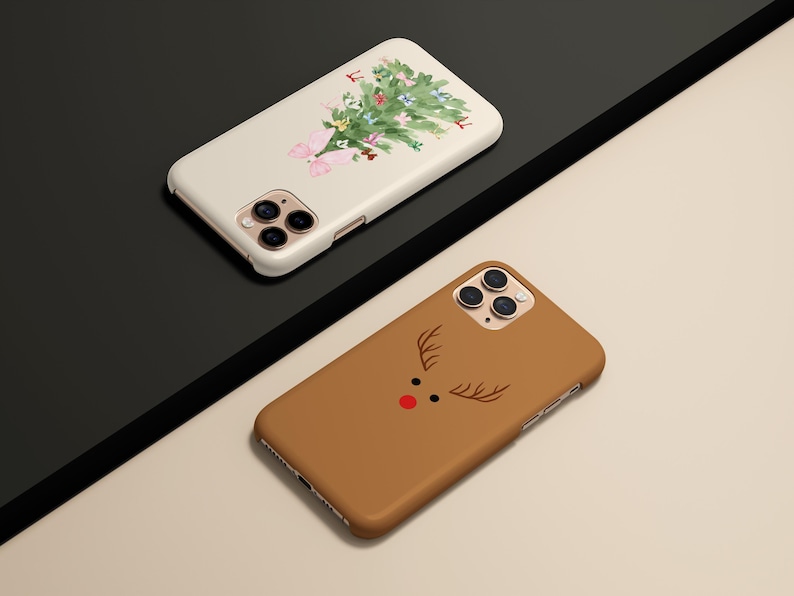 May include: Two phone cases. One is off-white with a watercolor Christmas tree design. The other is brown with a reindeer face design. Both cases have a glossy finish and are angled on a black and beige surface.